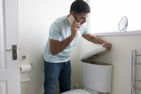 Man lifting a toilet bowl tank cover while talking on the phone